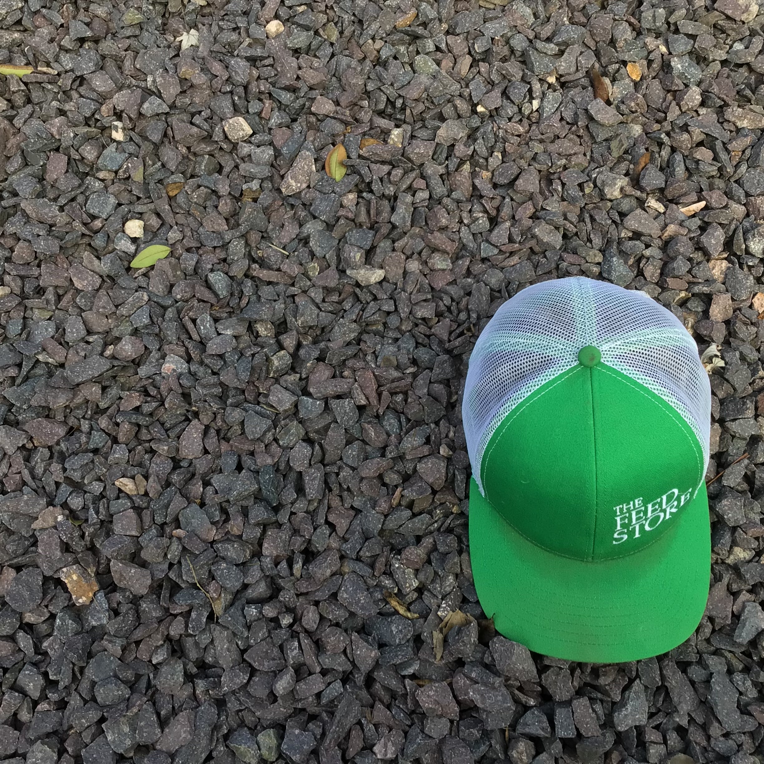 A green and white cap placed on a bed of dark gray bulk rocks, with the cap's brim showing the rocks underneath.