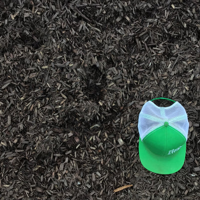 A green cap with a white mesh is placed on top of a pile of brown mulch.