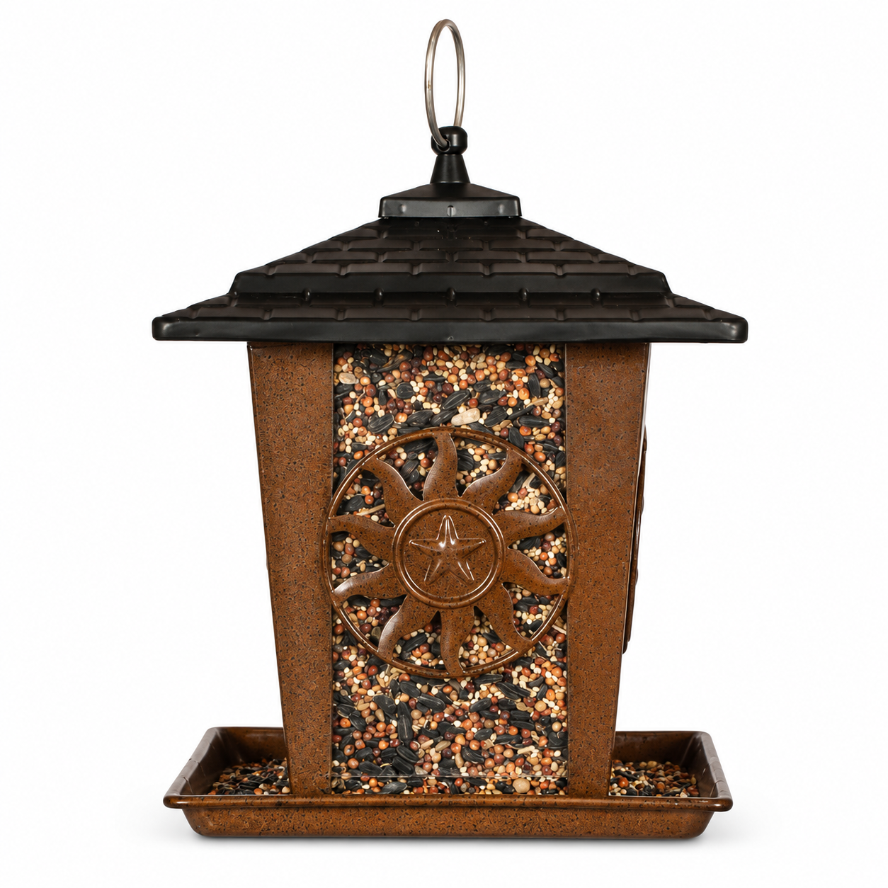 A brown and black metal bird feeder with a shingled roof, a central sunburst emblem with a star, and a tray at the bottom filled with mixed birdseed, shown on a white background.